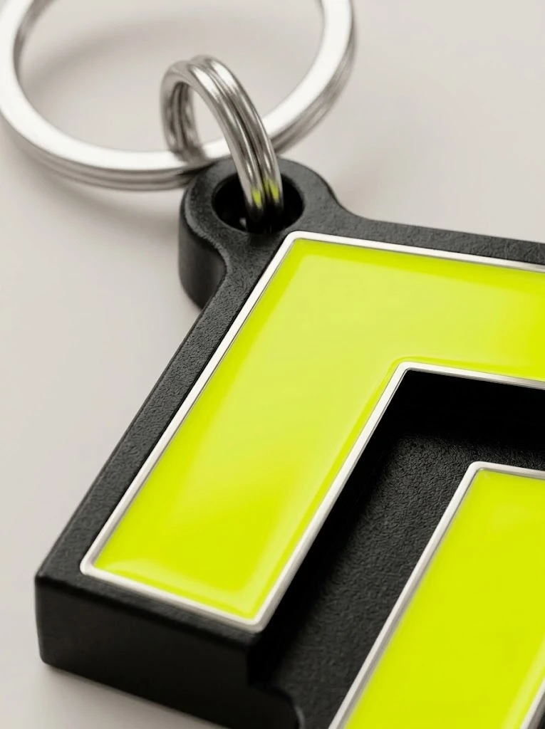 Gros plan du Porte-clé Galon : émail lime brillant cerné d’argent sur métal noir mat.